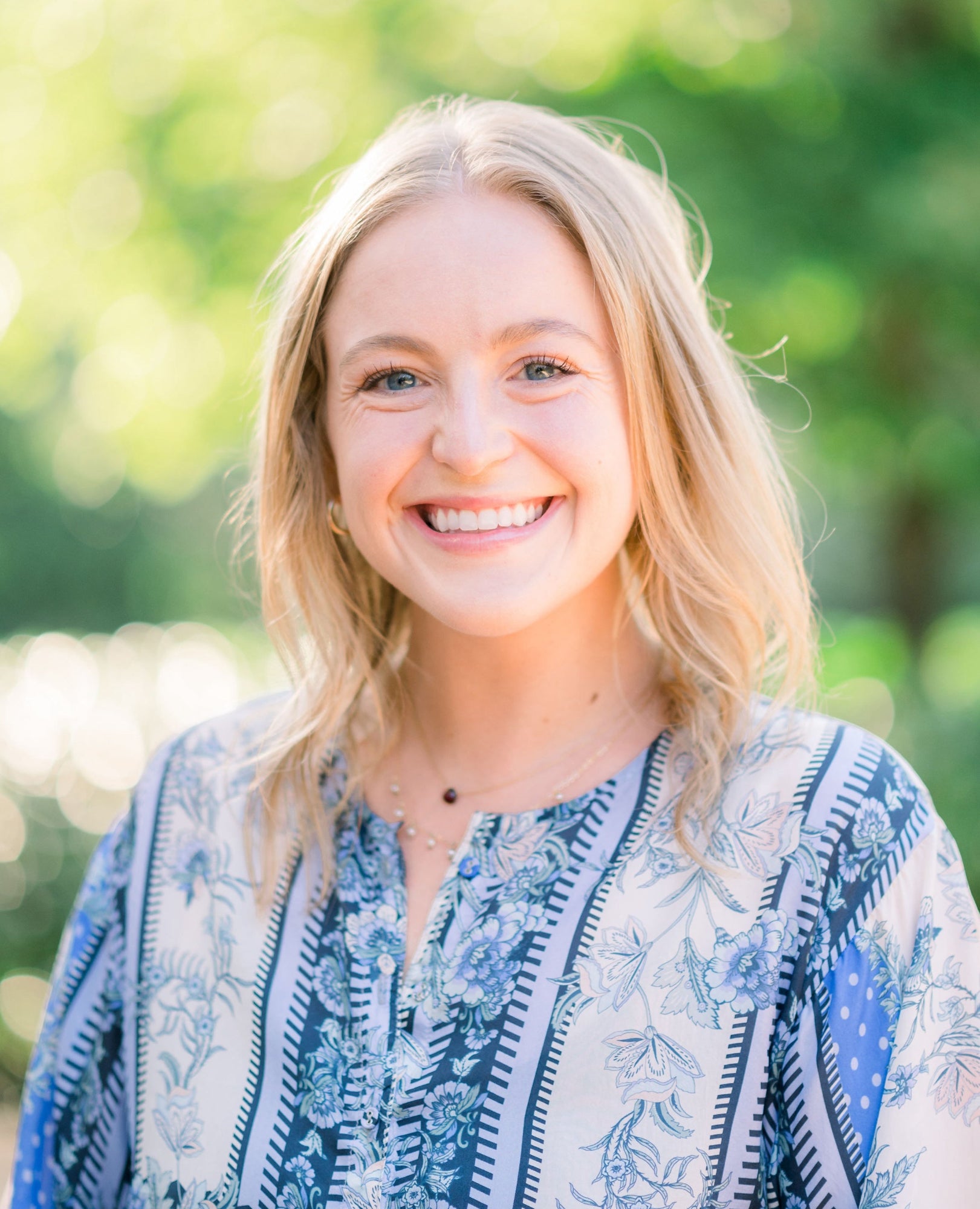 Woman with blonde hair wearing a blue and white patterned shirt outdoors.